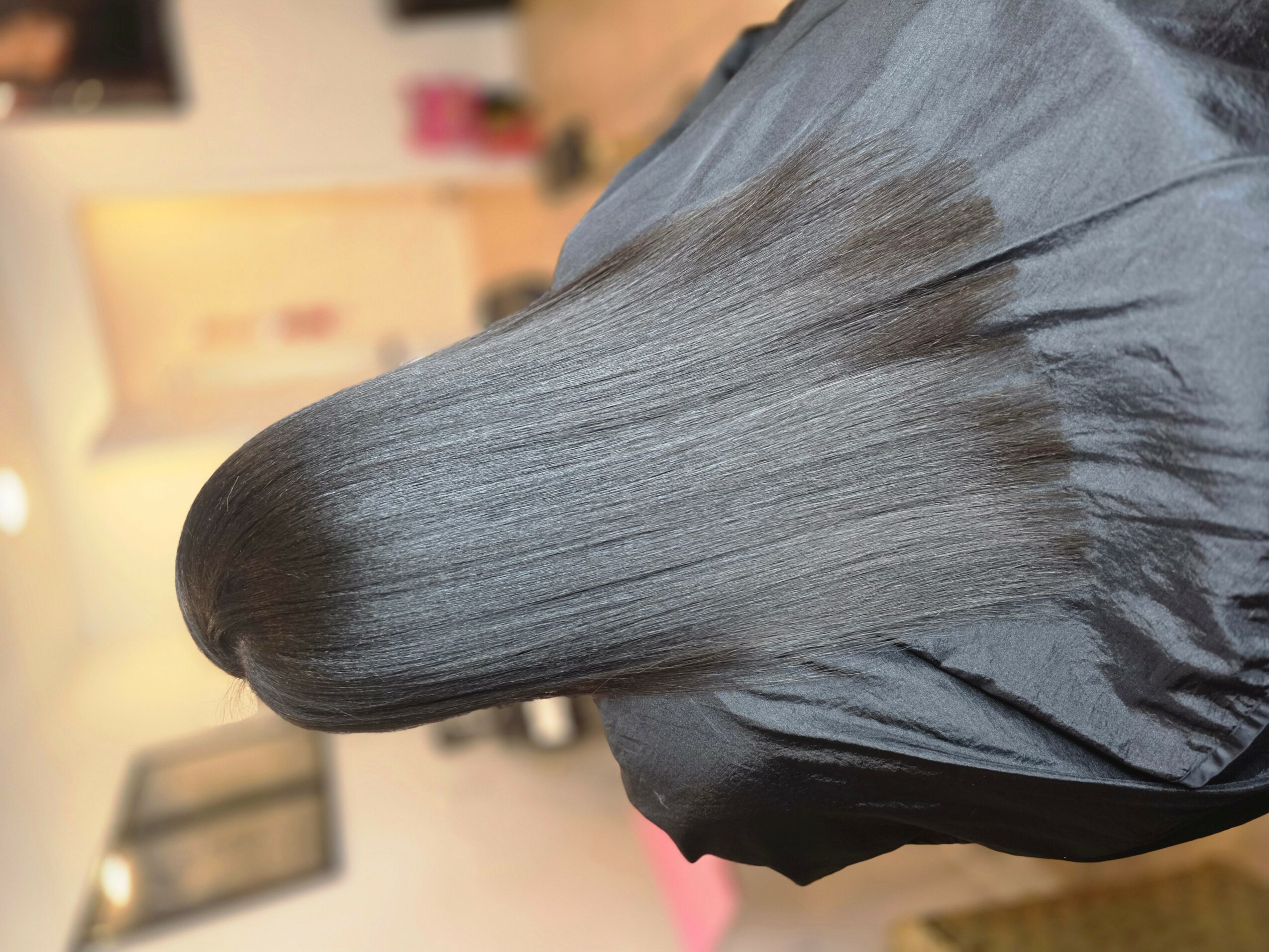 Person with long, straight, gray hair, wearing a dark cape, in an indoor setting.