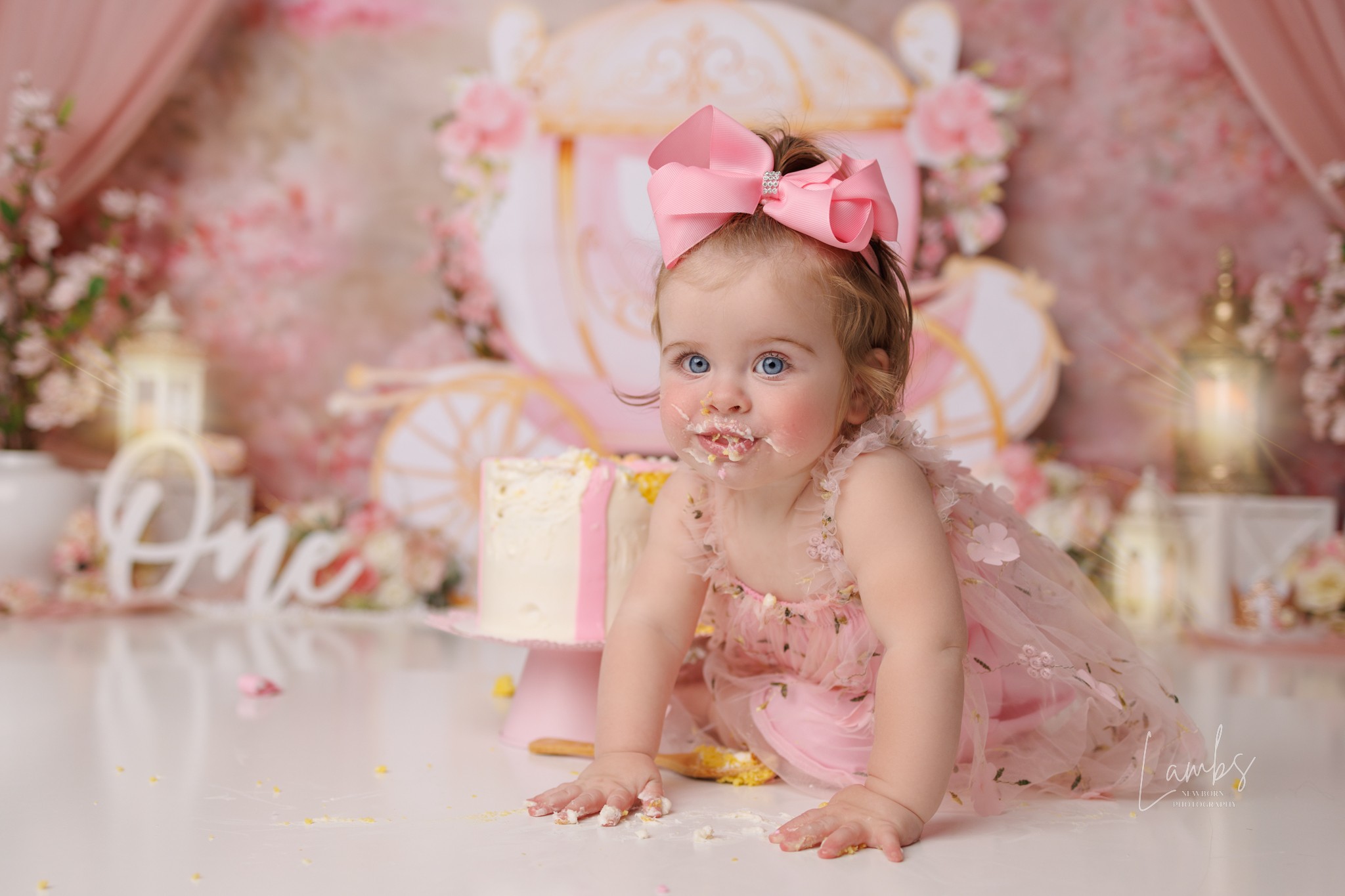 Baby girl with a pink bow headband crawling on a decorated table, pink and gold birthday theme background