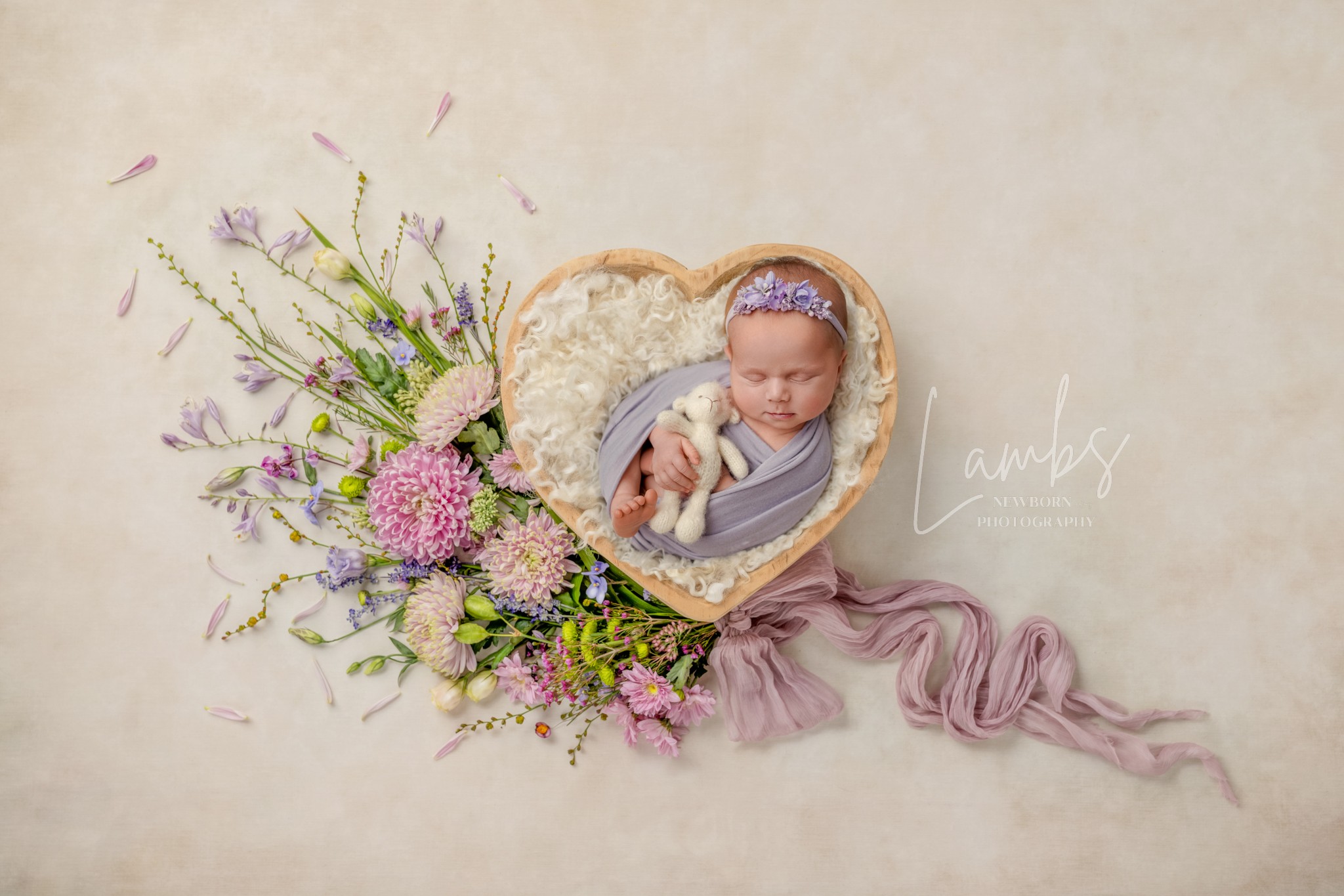Baby in a heart-shaped frame with flowers and a pink ribbon, on a light background.