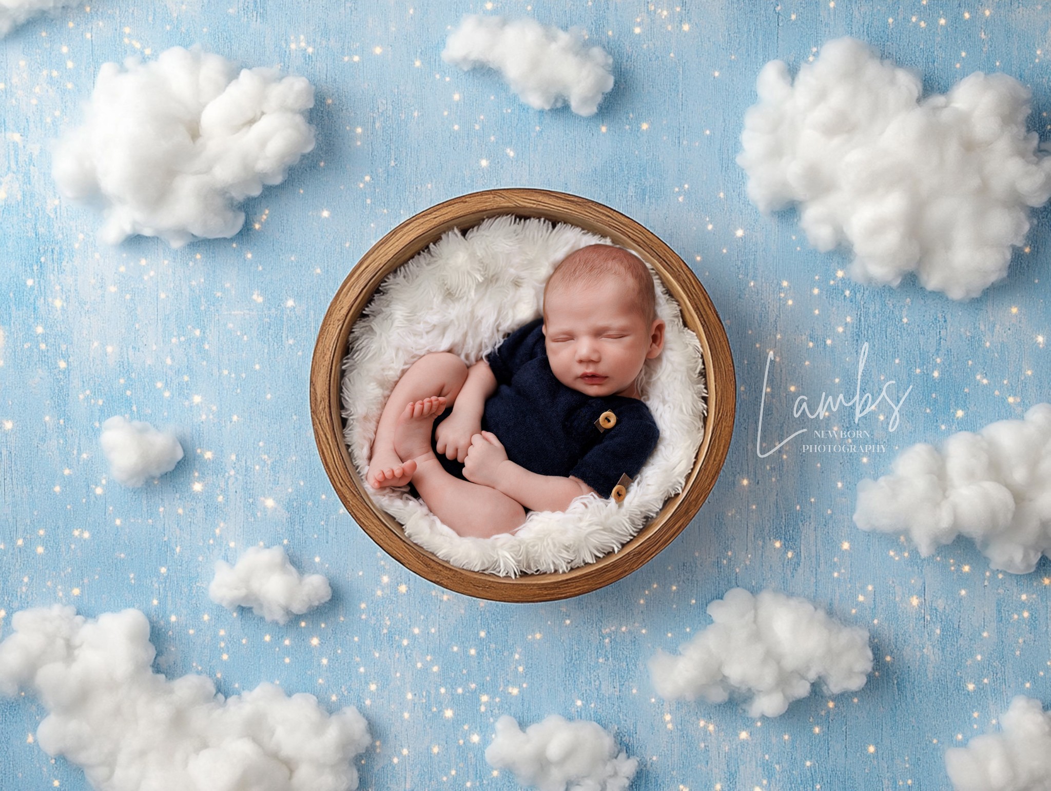 Baby sleeping in a round basket surrounded by clouds and stars on a blue background.