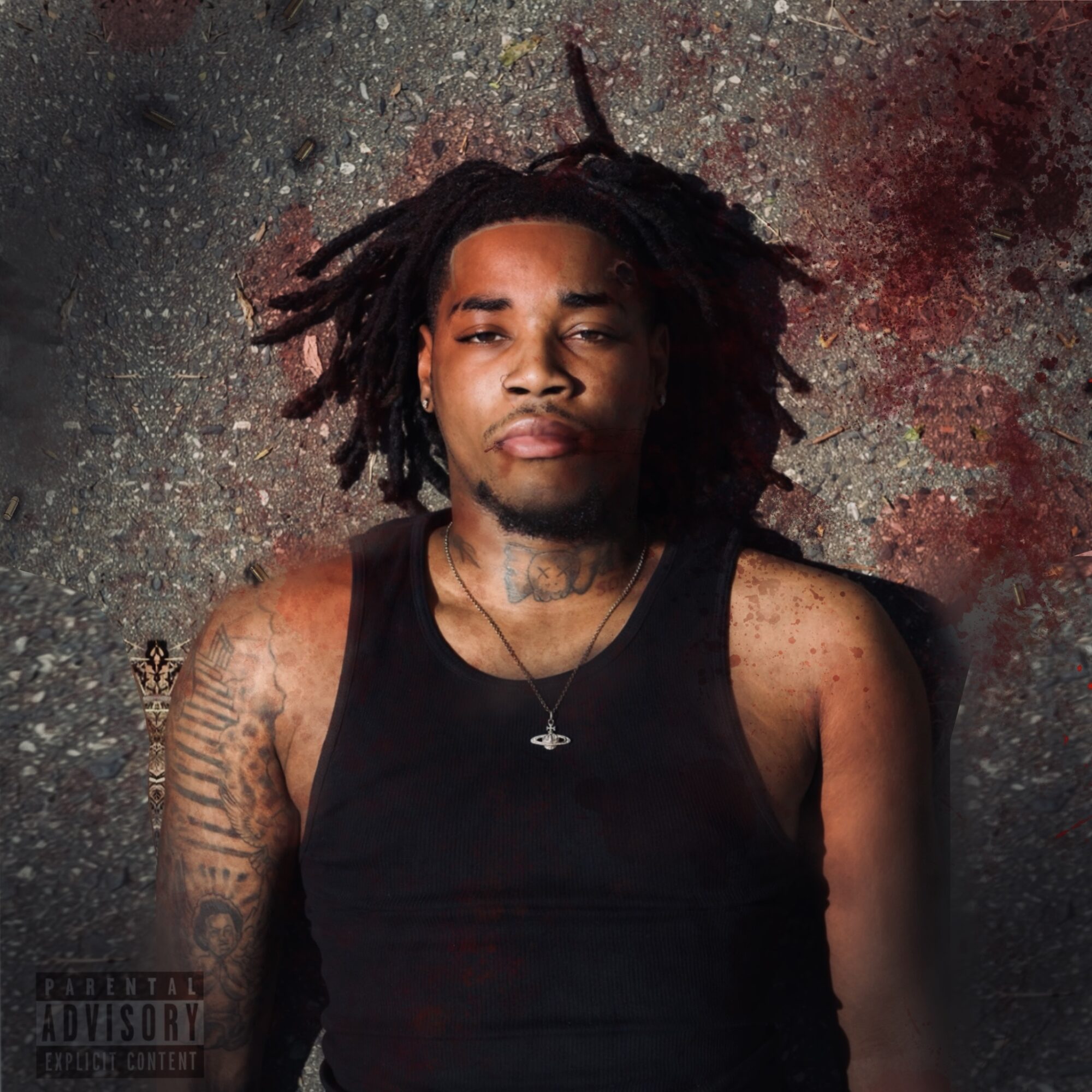 Young man with dreadlocks lying on ground, wearing a black tank top, tattoos visible on arms, with bloodstains nearby.