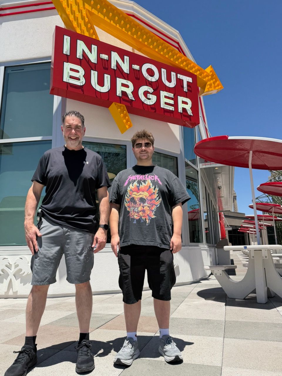 Two men standing outside a Burger King restaurant near an In-N-Out Burger sign, with red umbrellas and outdoor seating visible.