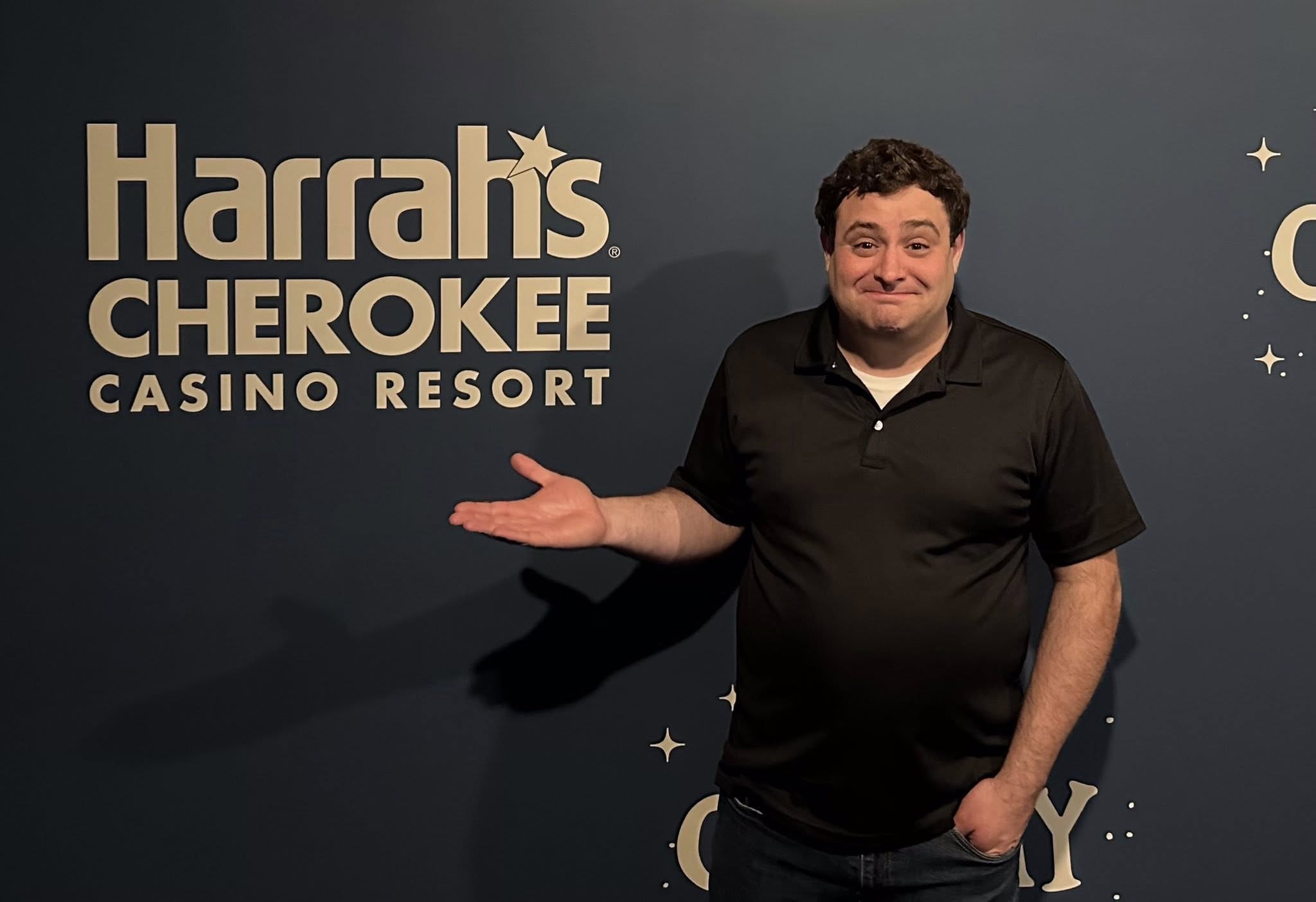 Man standing in front of Harrah's Cherokee Casino Resort sign, smiling, with one hand extended outward.
