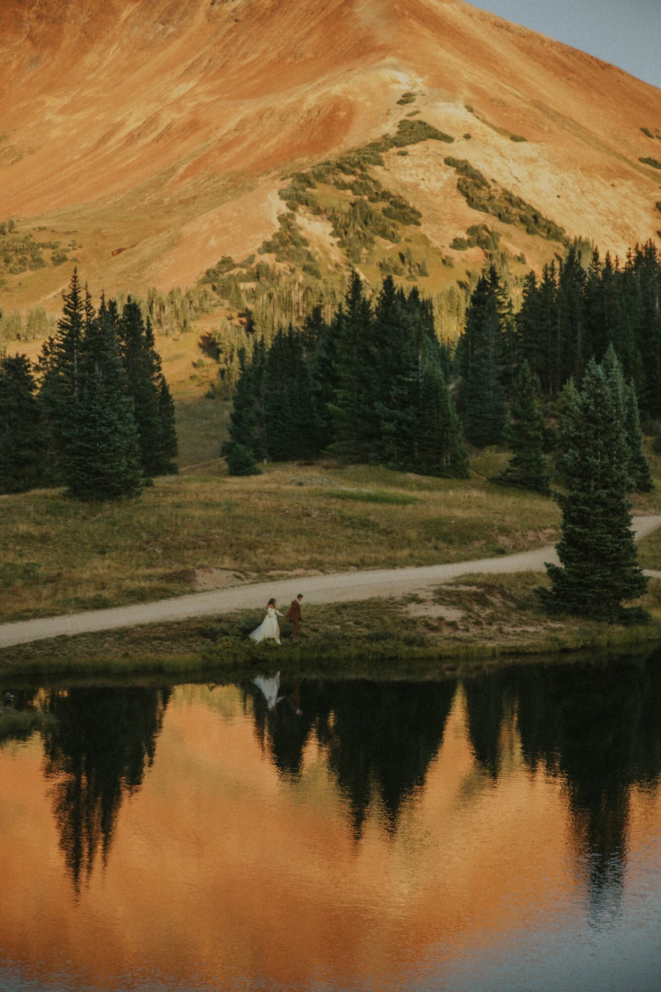 Scenic landscape with a mountain, trees, a river, and a person walking along the riverbank.