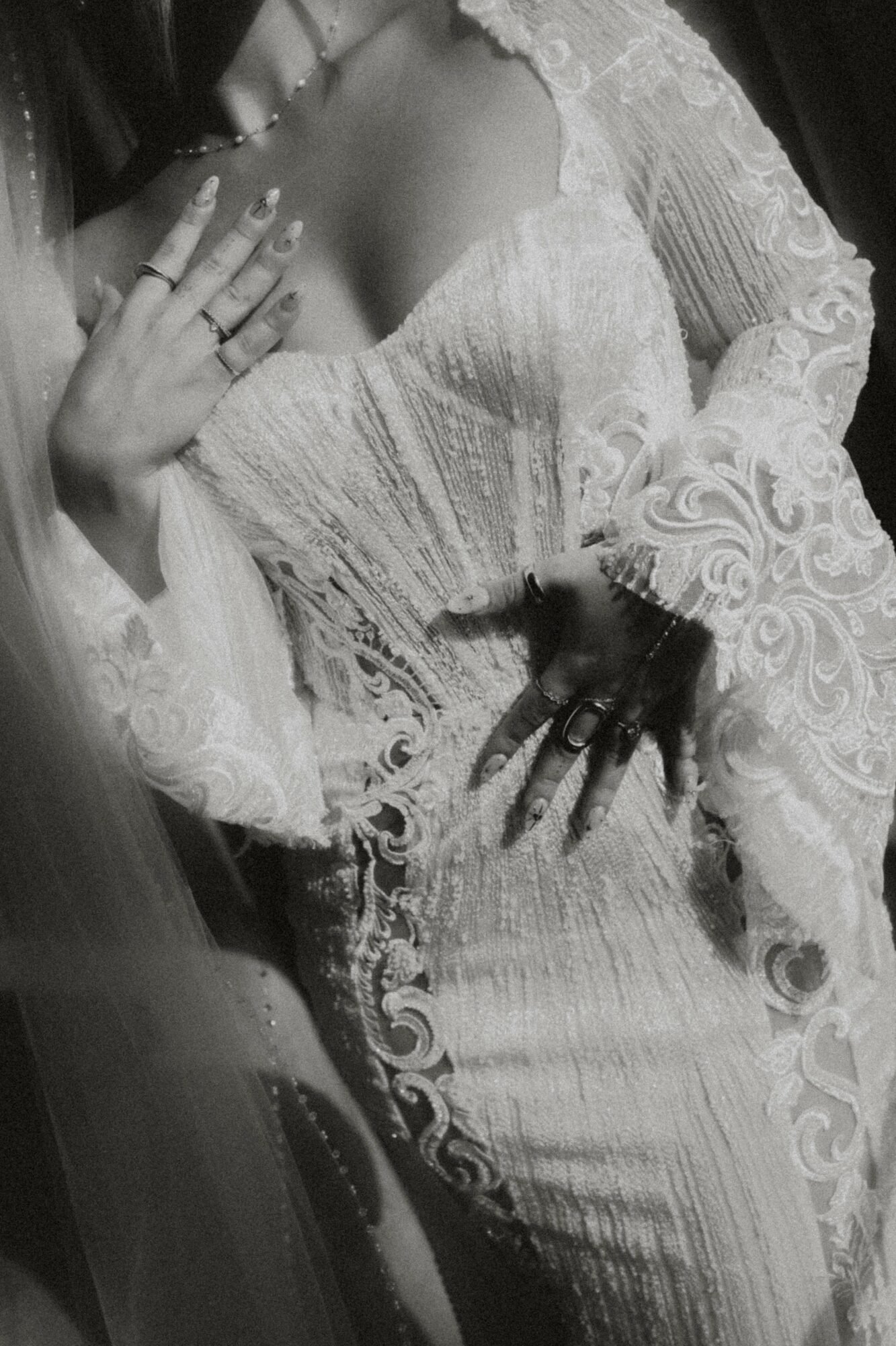 Person in a lace dress with hands on chest and waist, holding a phone, in black and white.