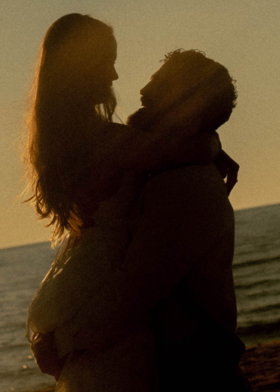 Silhouette of a couple embracing on a beach at sunset, with the ocean in the background.