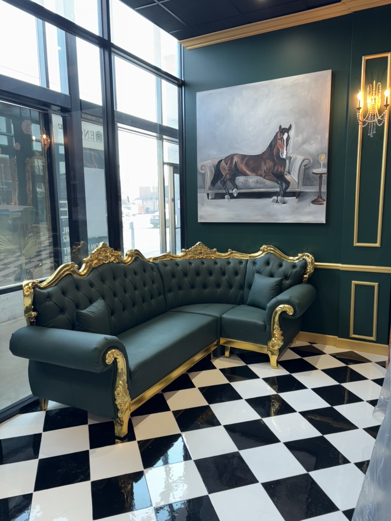 Luxurious green sofa with gold accents in a room with large windows, a painting of a horse, and black-and-white checkered floor.