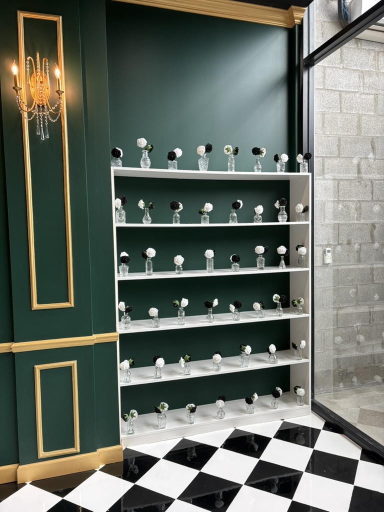 White shelf with multiple small objects, green wall, black and white checkered floor, and a glass window.