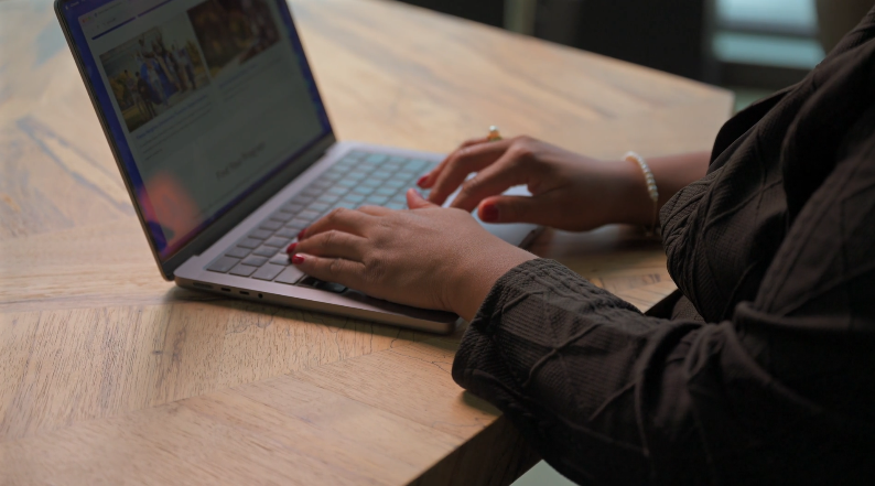 Person typing on a laptop at a wooden table, with a blurred background.