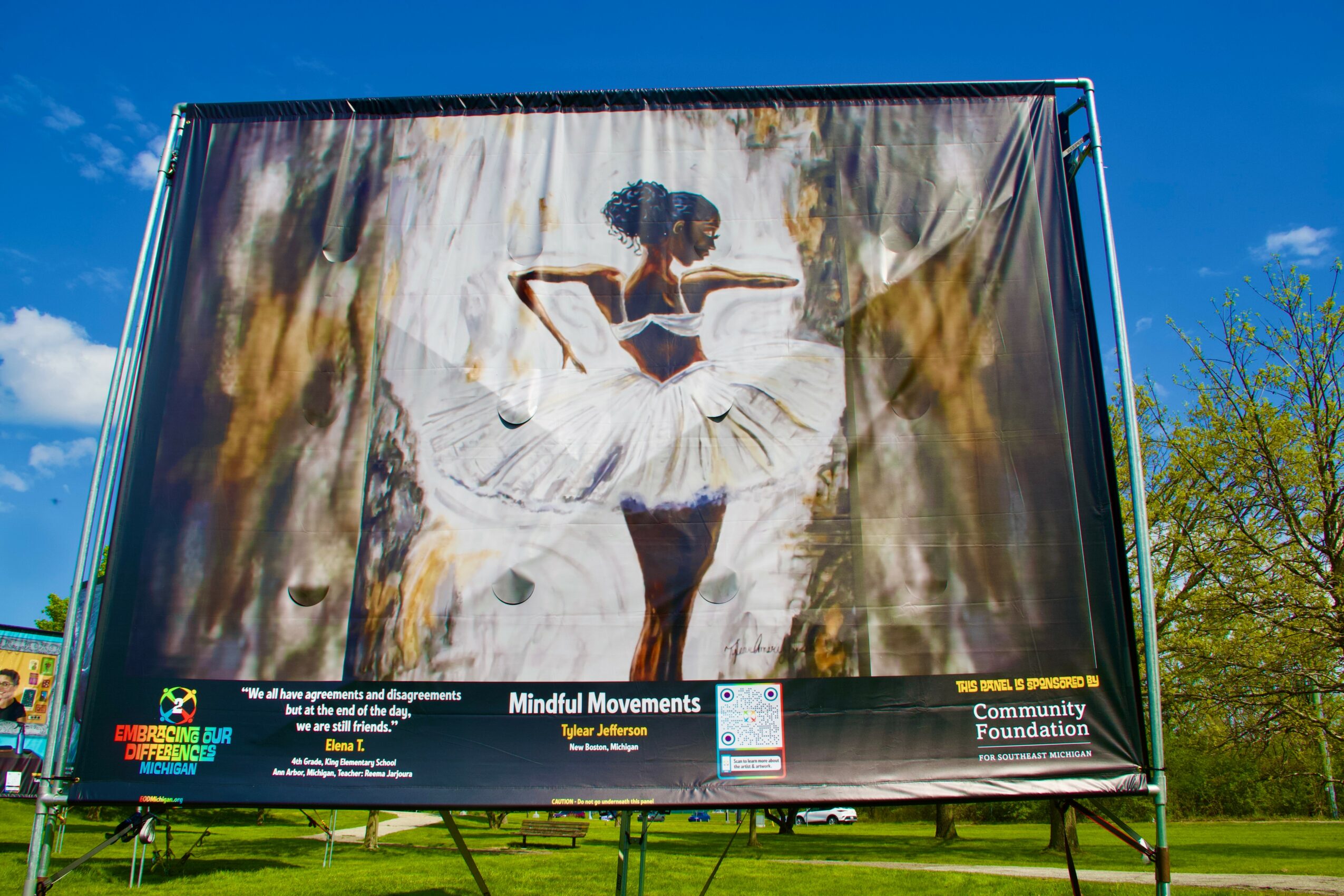 Billboard featuring a ballerina in a white tutu performing a dance pose outdoors against a blue sky with trees in the background.