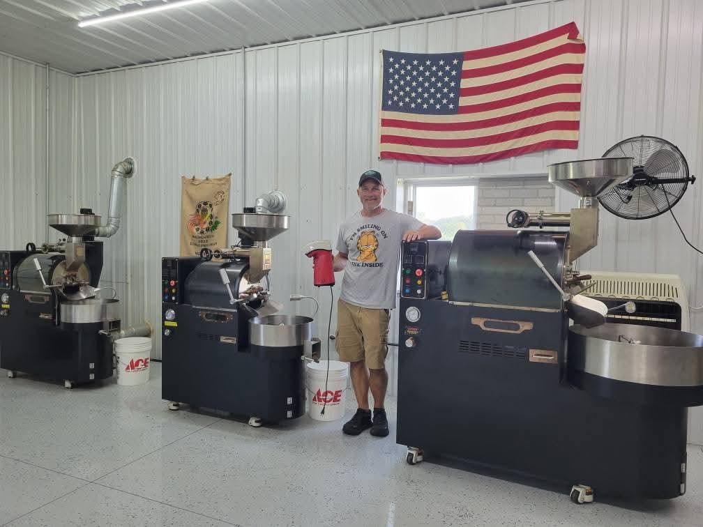 Person standing between two large machines inside a room with an American flag on the wall.
