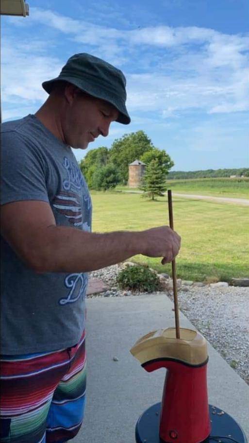 Person wearing a hat and striped shorts outdoors, holding a stick near a red object, with a grassy field and blue sky.
