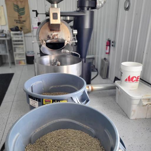 Grain roasting machine with buckets of grains, a white container, and a workshop background.