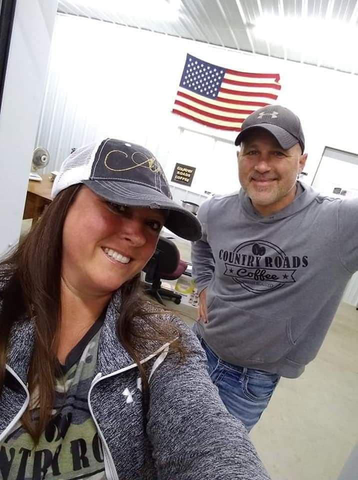 Two people smiling in an indoor setting with an American flag hanging above them.