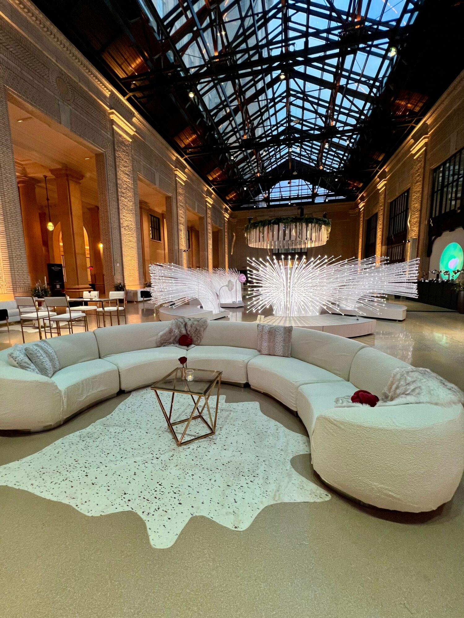 Indoor space with a large, curved white sofa, a small glass table, and decorative elements, under a glass ceiling.