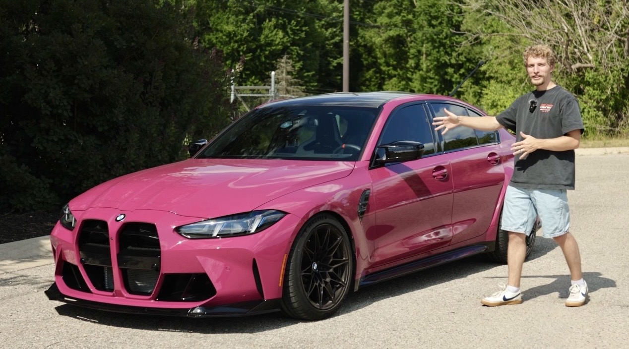 Person standing next to a pink sports car outdoors, pointing at the vehicle, with trees in the background.
