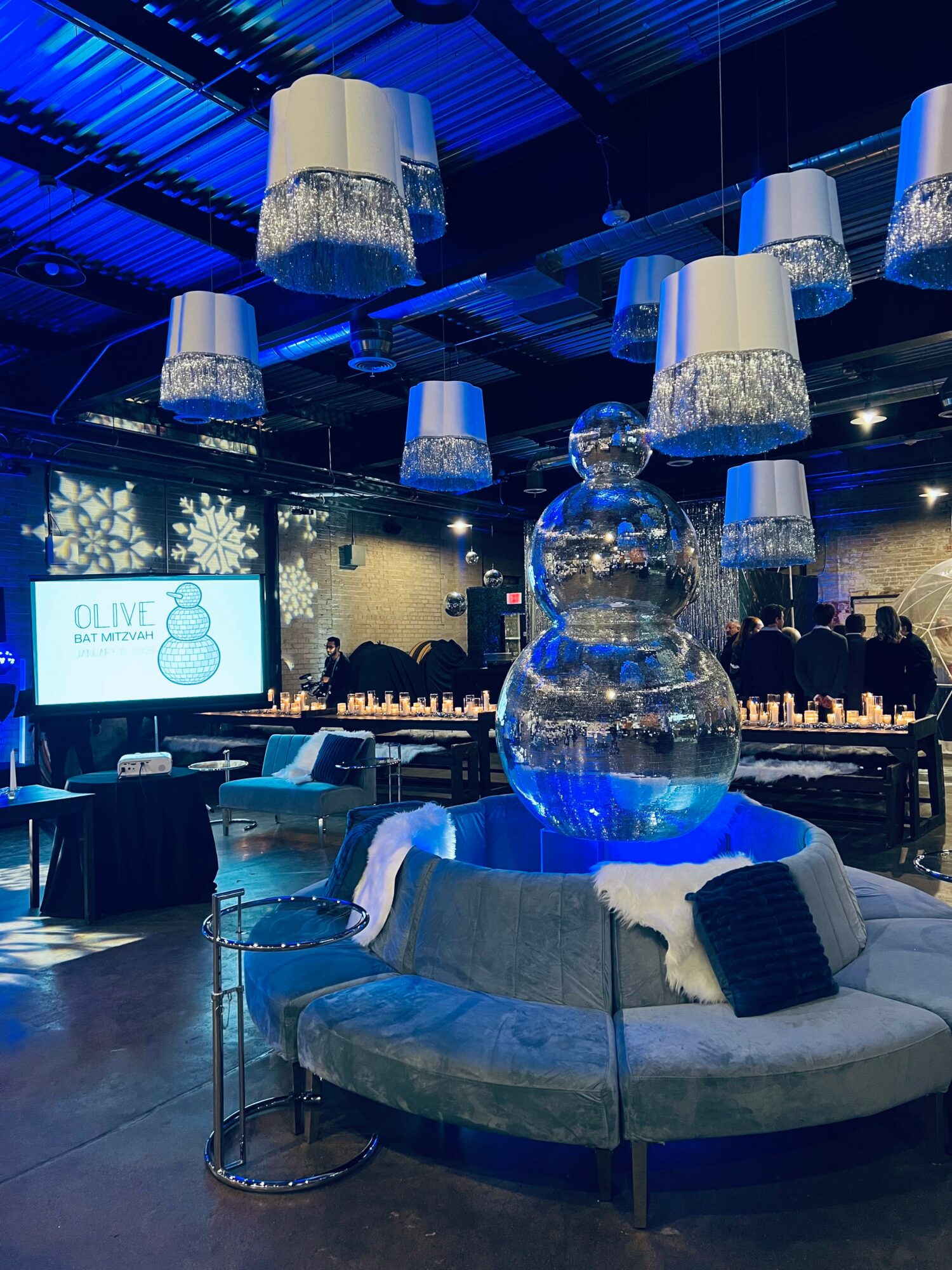 Elegant event space with hanging lamps, a large glass snowman sculpture, and a presentation screen, decorated in blue and white.