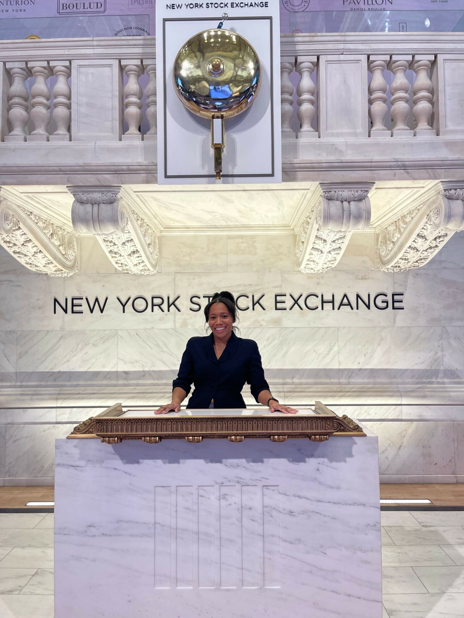 Man in dark suit at a desk in a grand marble room with a sign reading 'New York Stock Exchange'.