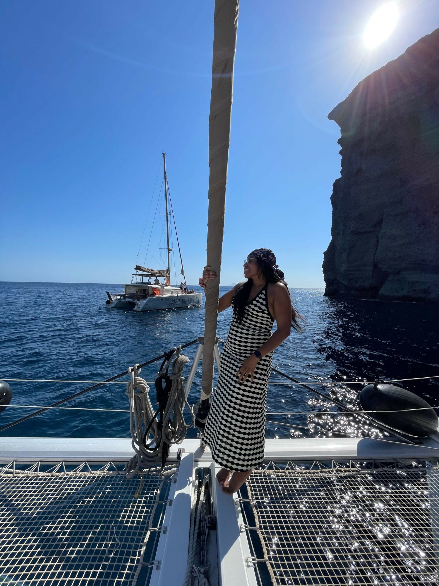Woman in a striped dress standing on a boat deck with water and boats in the background.