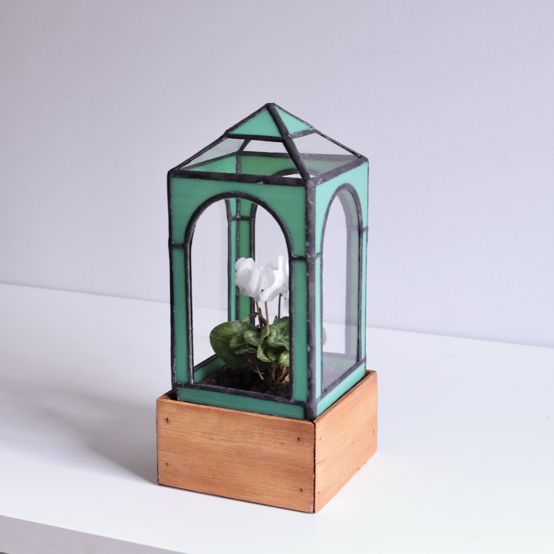 Glass terrarium with a white flower inside, mounted on a wooden base, against a plain background.