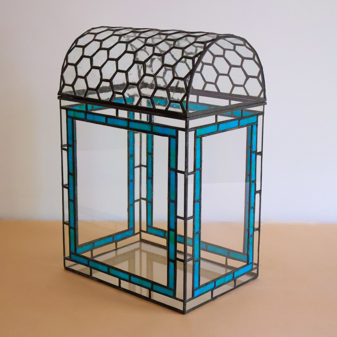 Glass and metal decorative object with a hexagonal pattern on top, on a wooden surface, against a plain background.