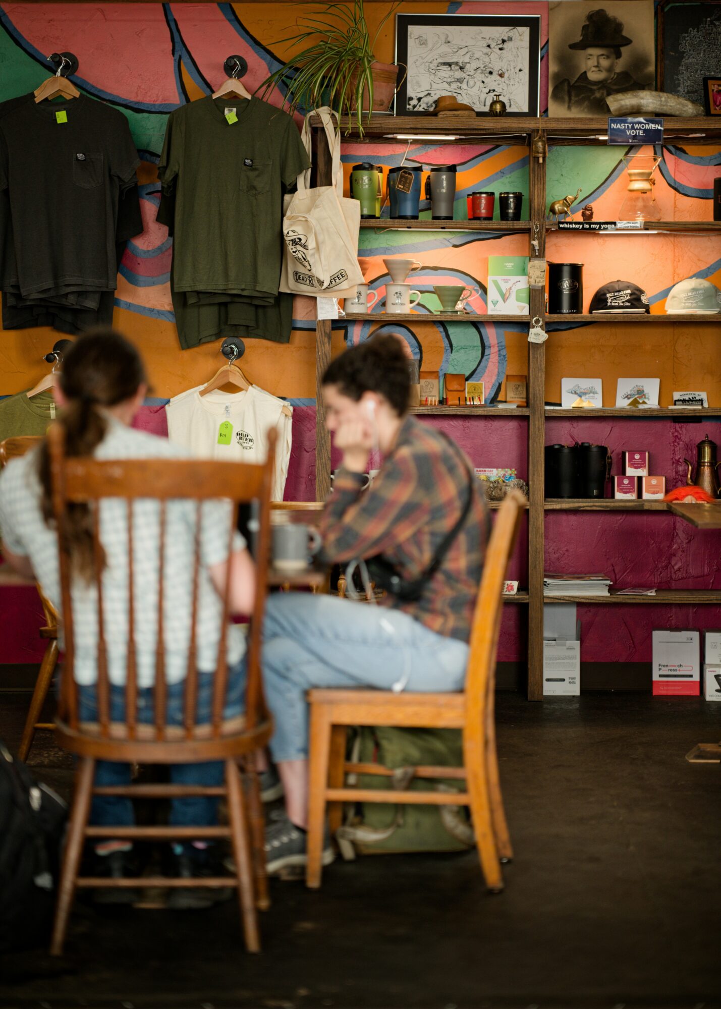 Two people sit at a table in a store with clothing and accessories on shelves behind them.