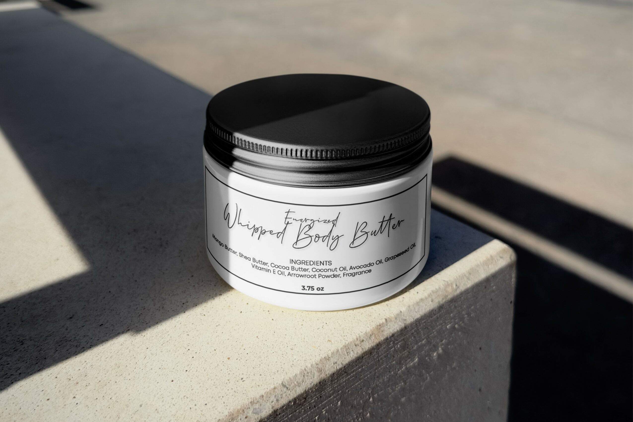 Container of body butter with black lid on concrete surface, shadow cast nearby, outdoors, minimal background.