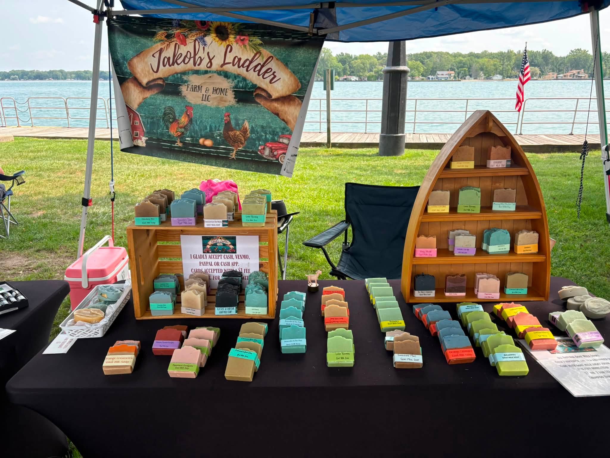 Soap display at outdoor booth with colorful soap bars, a banner, and a lake in the background.