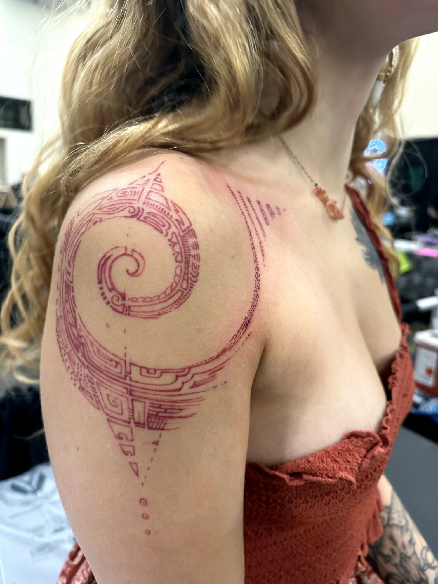 Tattoo of a spiral design on shoulder and upper arm, with intricate lines and patterns, in pink ink.