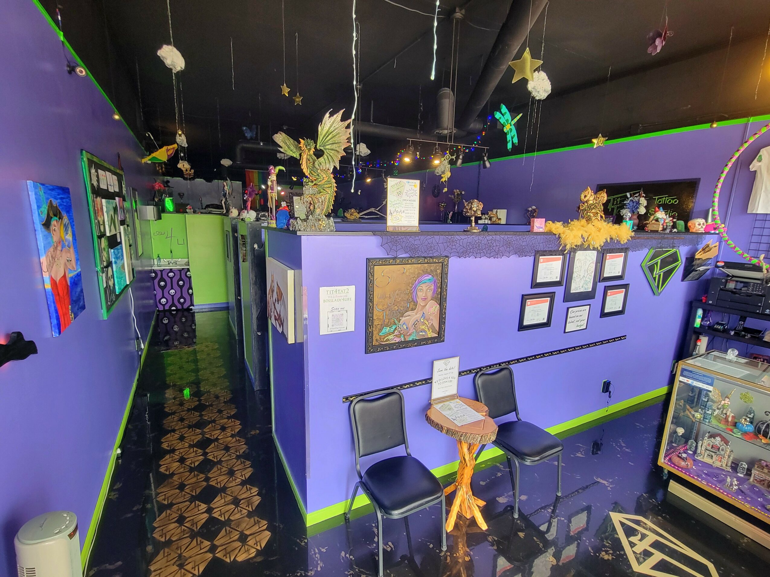 Interior of a colorful room with purple and green walls, decorated with hanging ornaments, framed pictures, and a small table with two chairs.