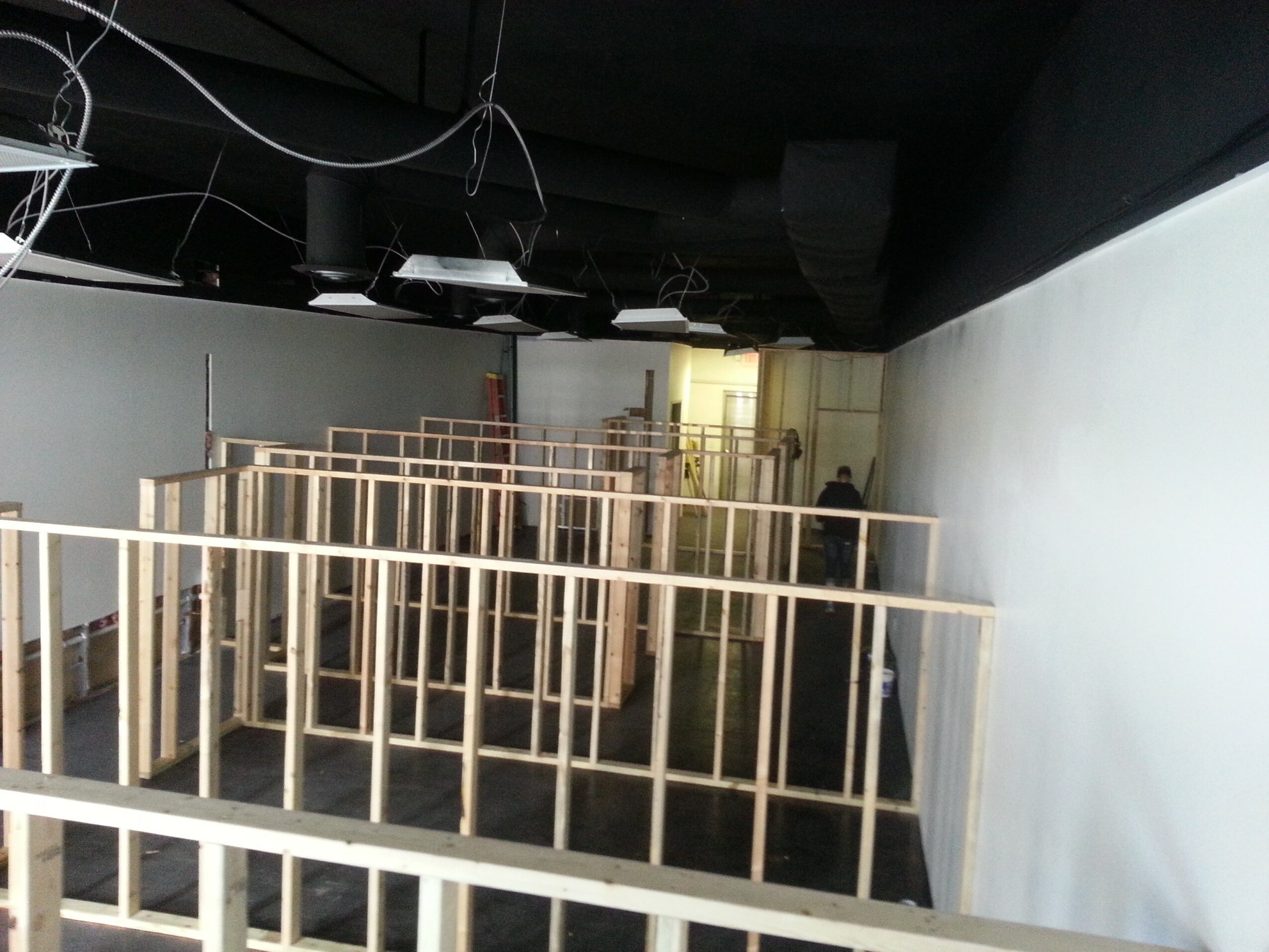 Interior space with wooden frames and a white wall, ceiling with exposed wires, and a dark ceiling area.