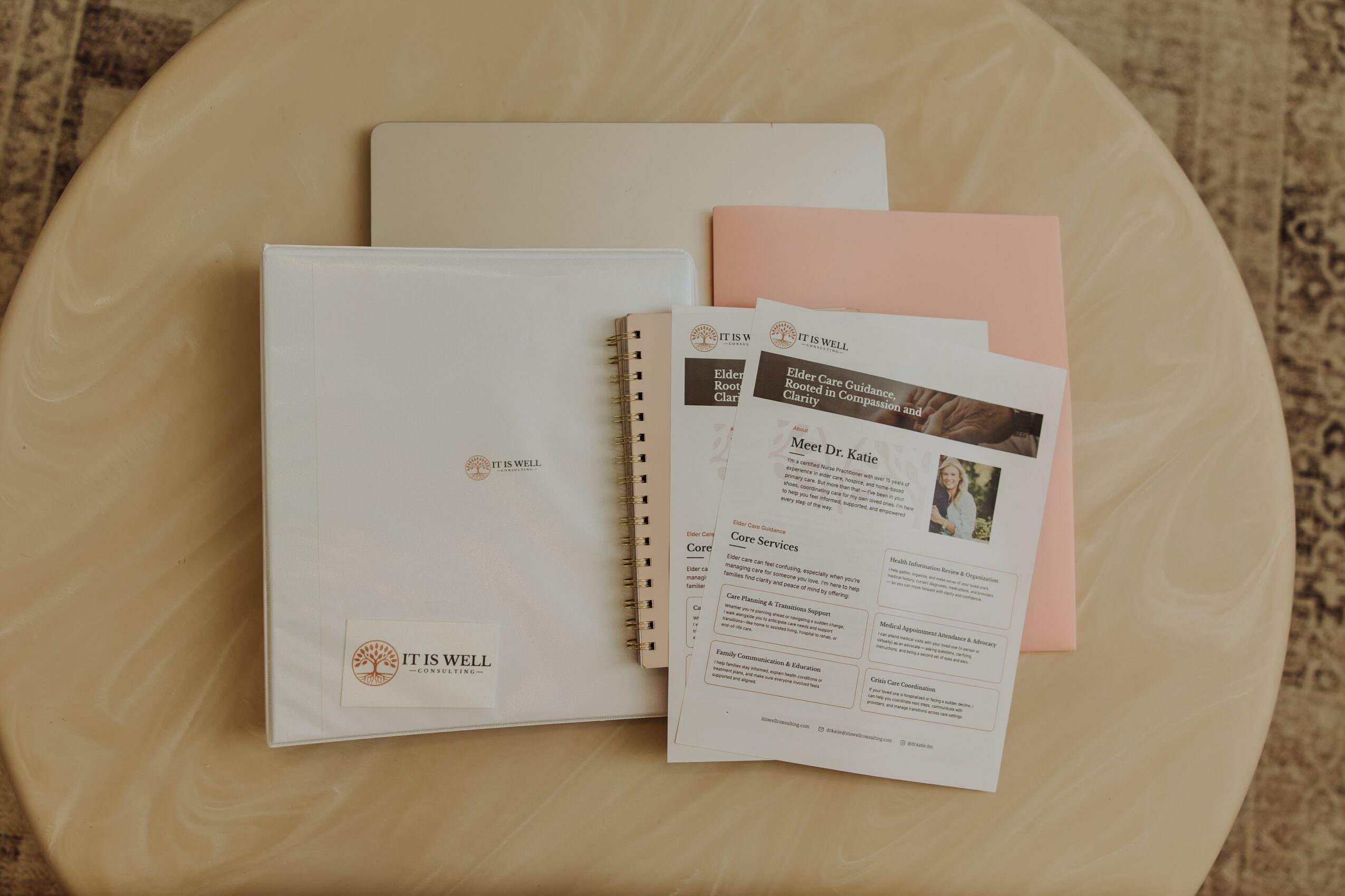 Documents and folders on a round wooden table, including a white folder, pink folder, and printed papers.