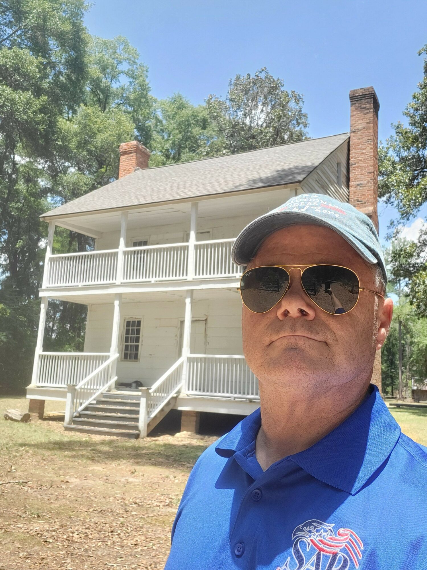 Man wearing sunglasses and a headband outdoors with a white house and trees in background.