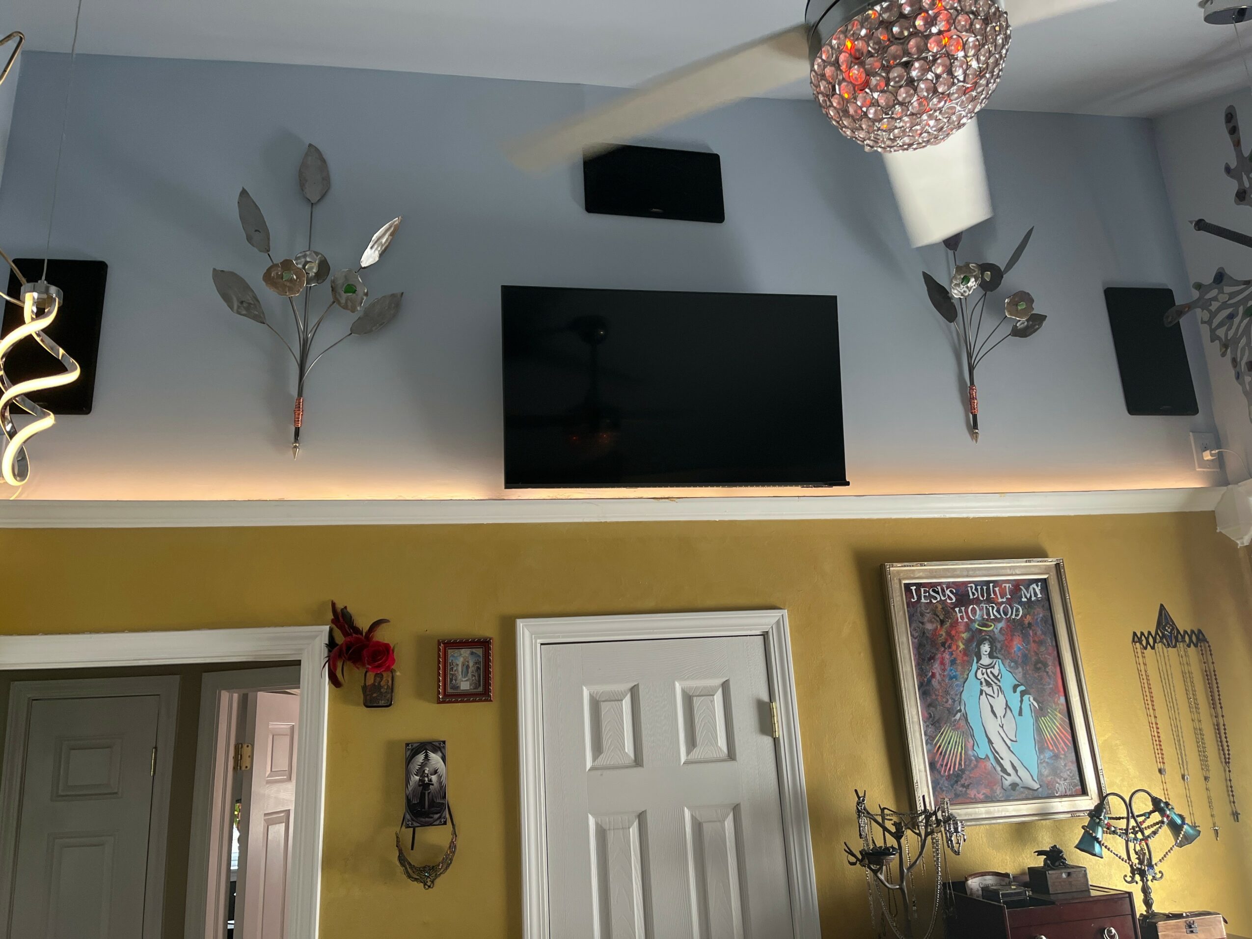 Living room with wall-mounted TV, decorative wall art, and a door, with a colorful framed picture and a chandelier.