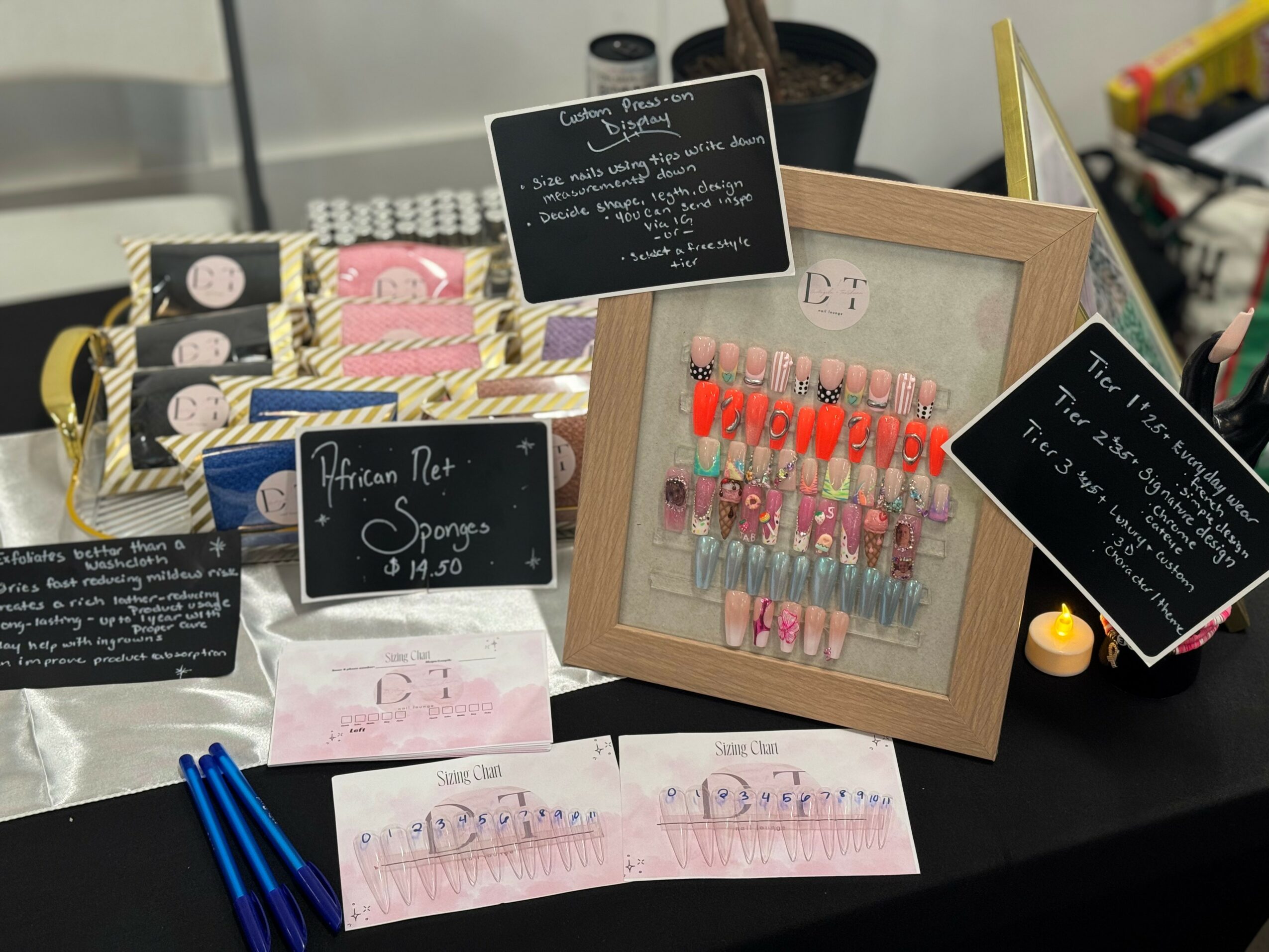 Display of nail polish samples, signs, and decorative items on a black table, with a framed nail color chart in the center.