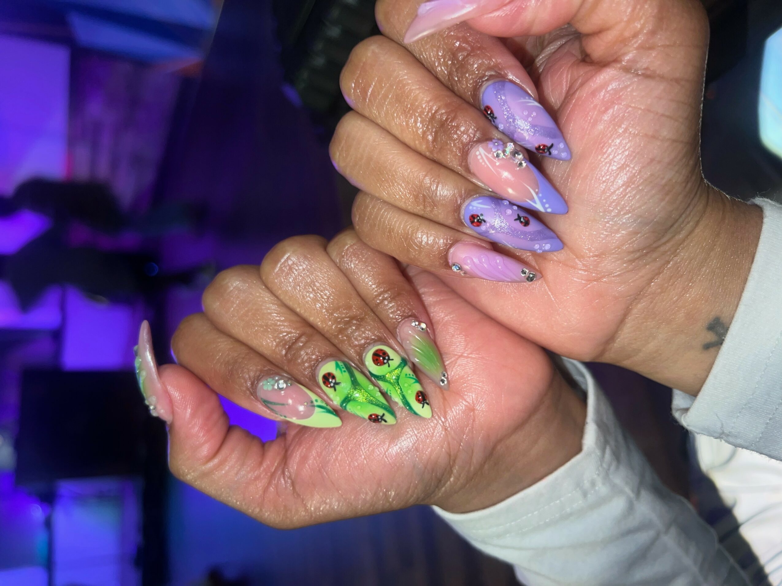 Two hands with long, decorated nails, one with purple and the other with green designs, held together.