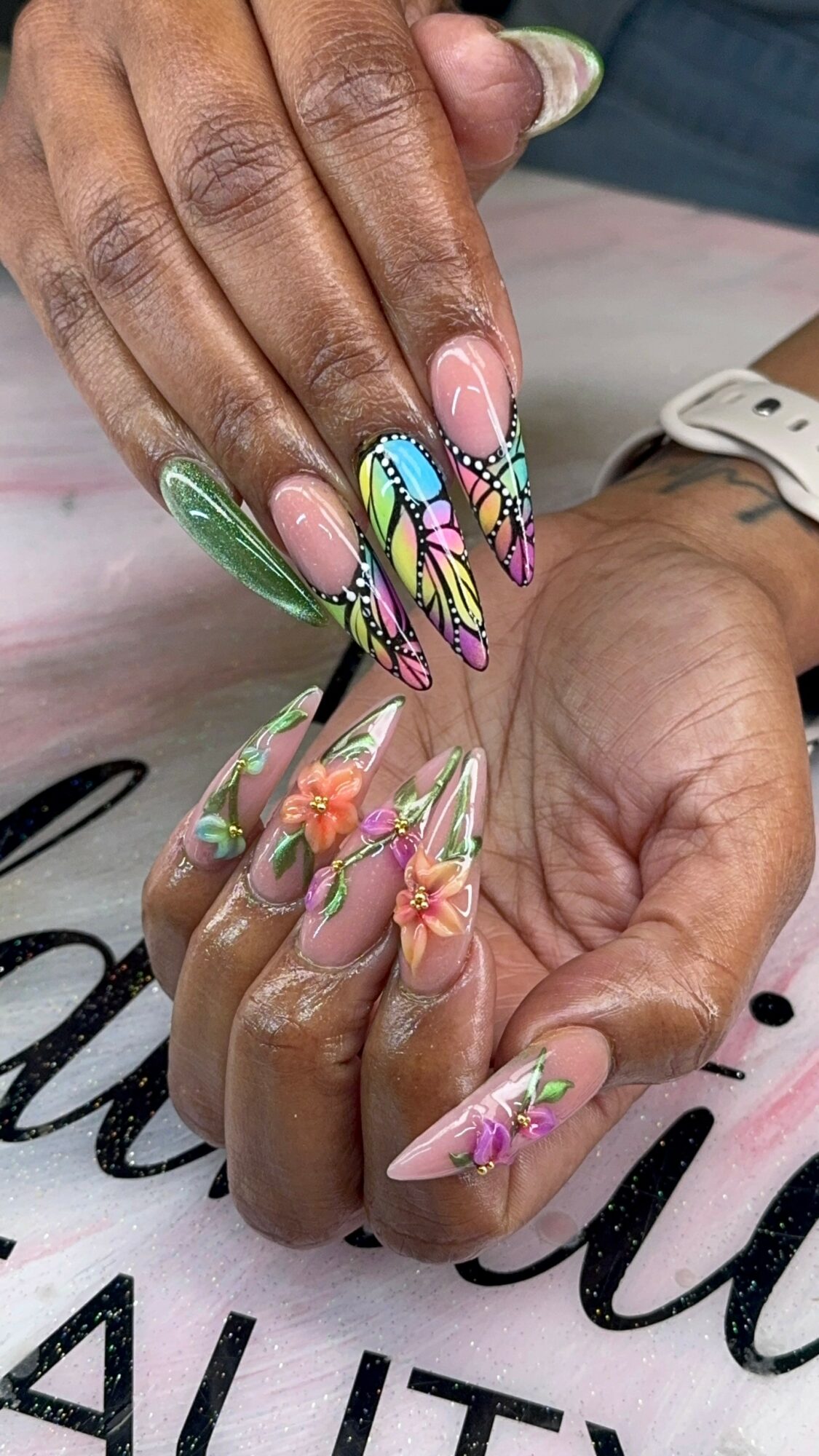 Close-up of hands with colorful, intricate nail art featuring floral and butterfly designs, some nails with pink and green accents.