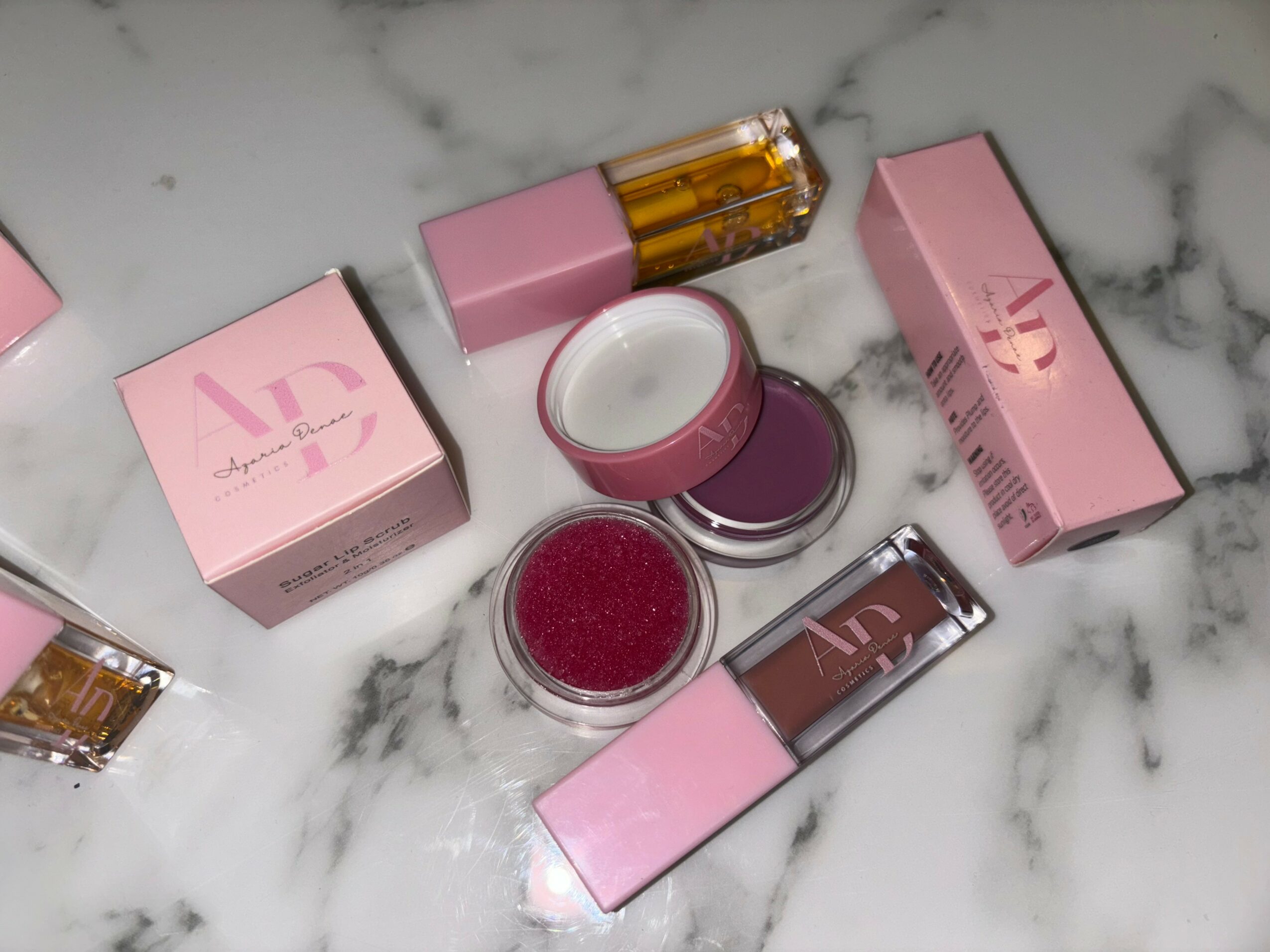 Various makeup products, including lip gloss and lip balm, arranged on a marble surface.