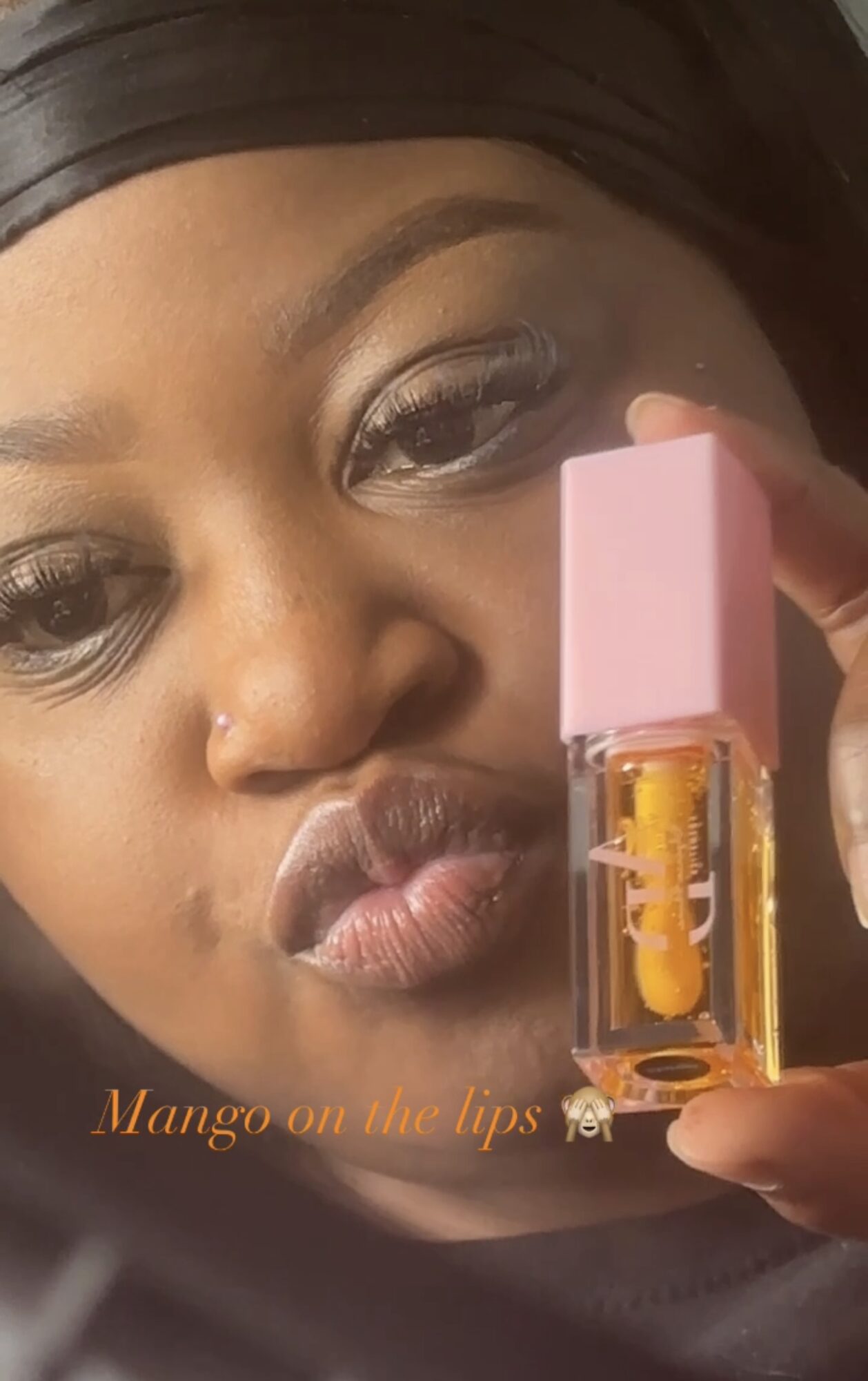 Close-up of a woman with dark hair holding a pink-lidded lip gloss tube near her lips.