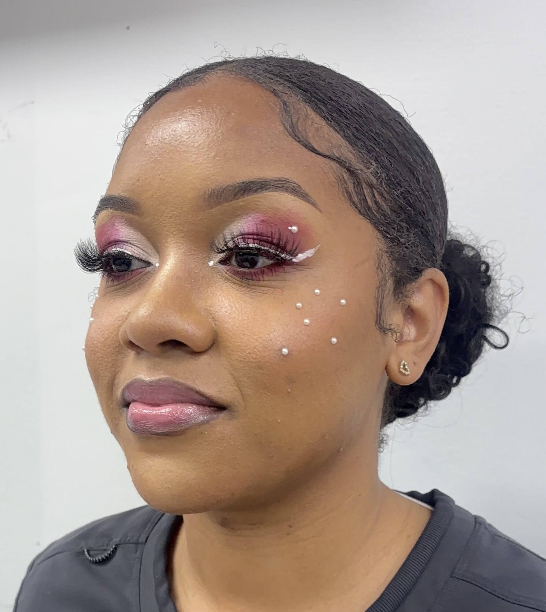 Close-up of a woman with styled hair, pink eye makeup, and small white decorative dots on her face.