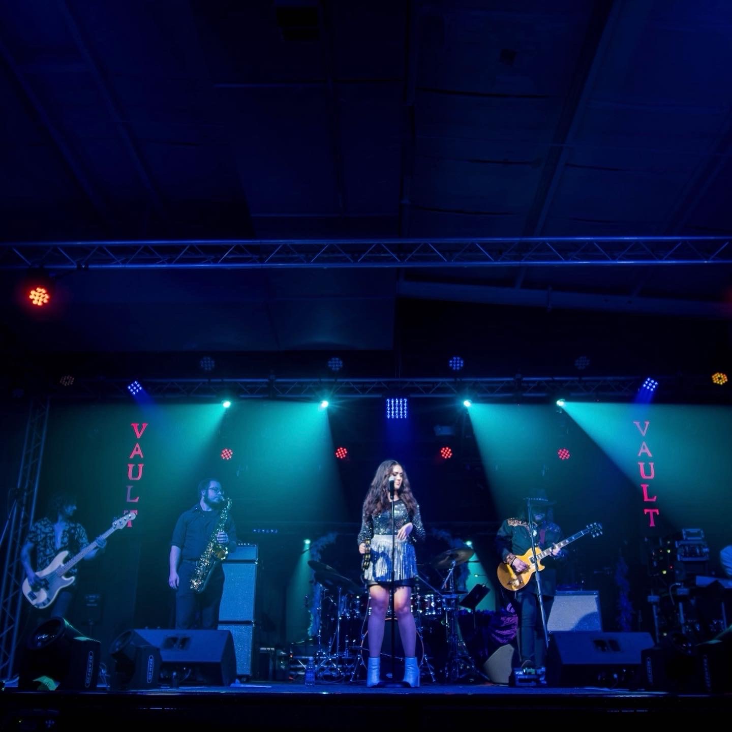 Band performs on stage with colorful lighting, a female singer in the center, and instruments around her.