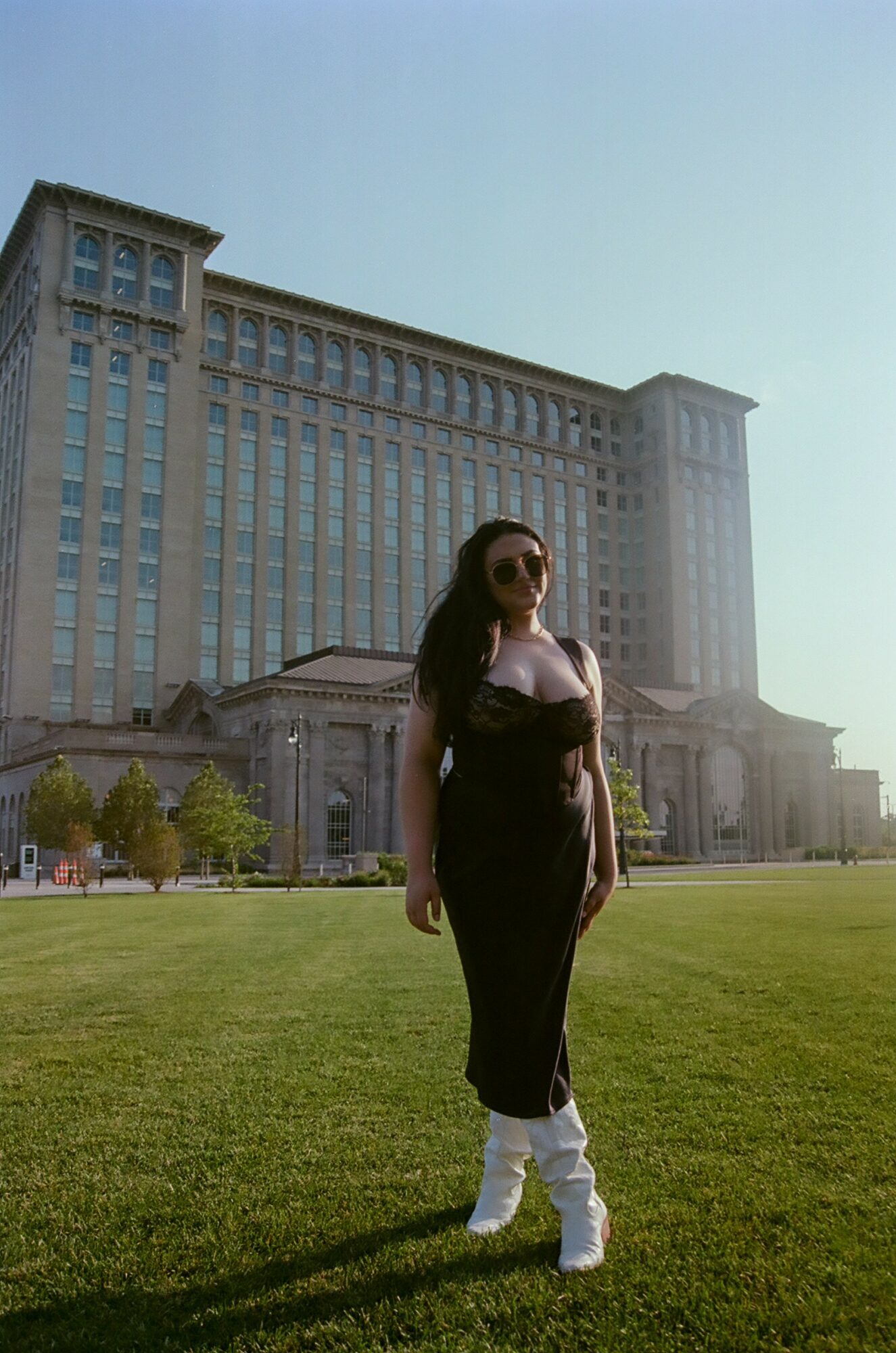 Woman standing on grass in front of a large building with columns and tall windows, sunny day.