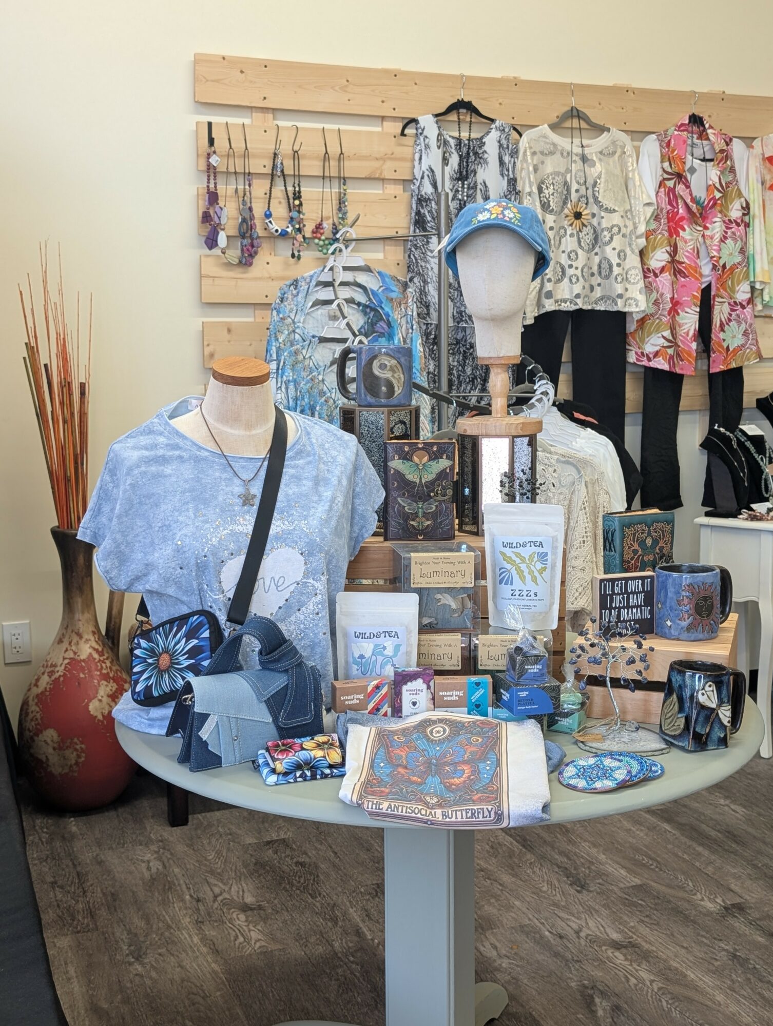 Display of blue and white clothing, accessories, and home decor items in a retail store, with a wooden wall and mannequins.