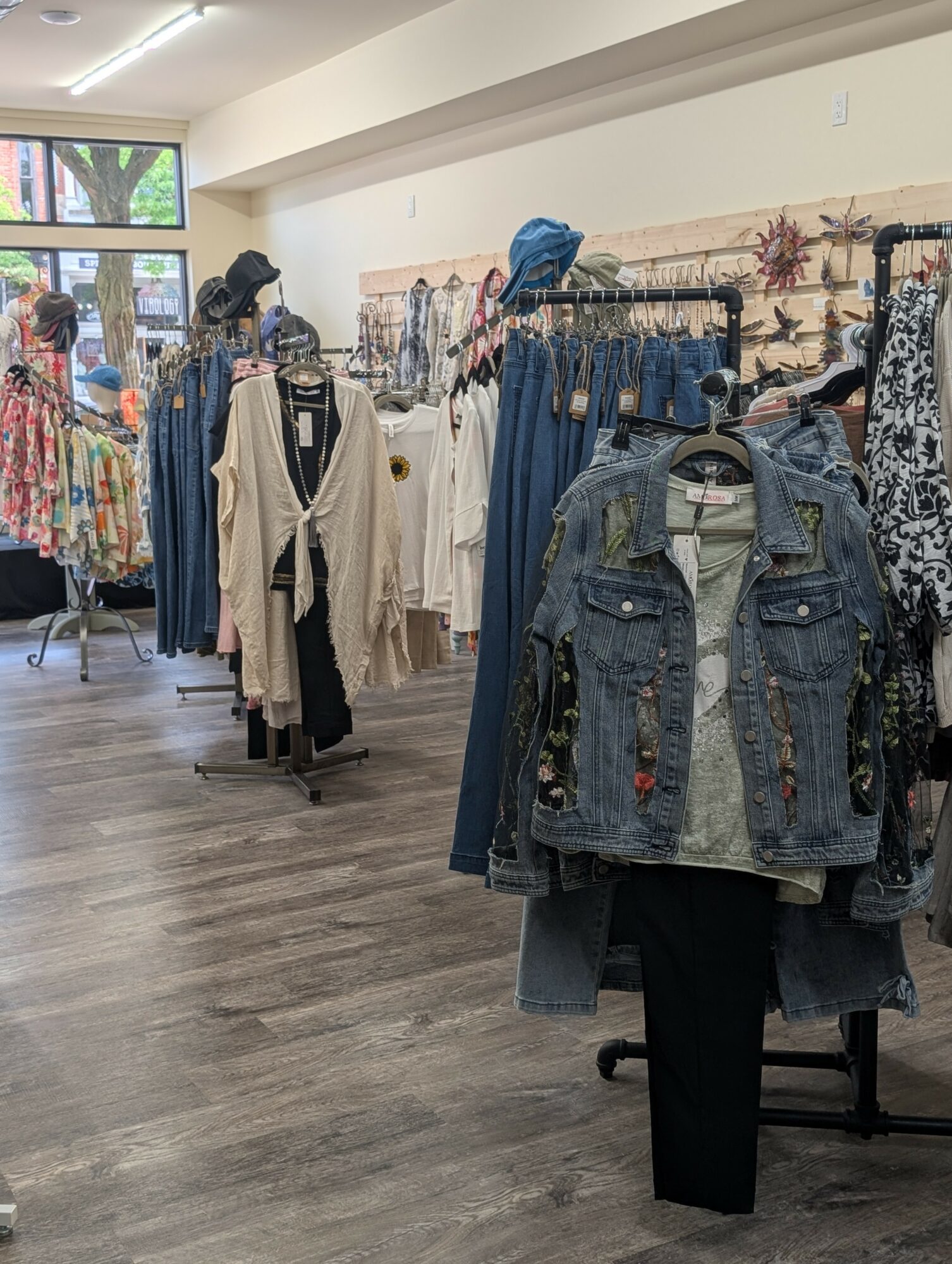 Clothing store interior with racks of dresses, jeans, and jackets, and a person browsing near the window.