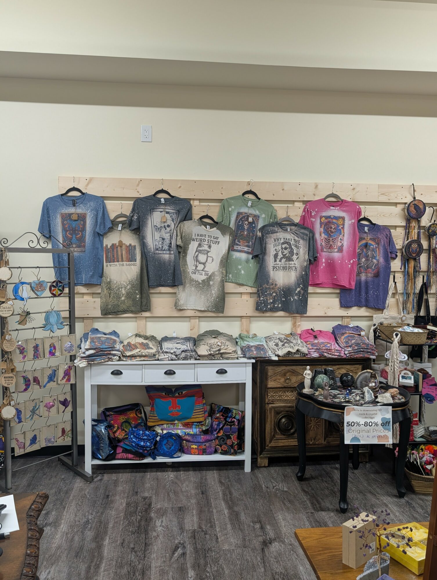 Display of colorful backpacks and accessories on shelves and tables in a store, with a wooden floor and light-colored wall.