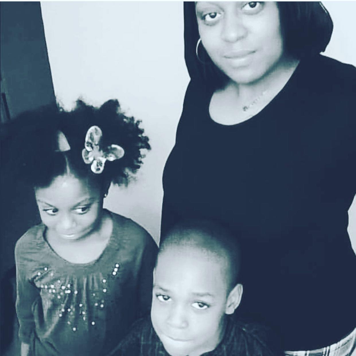 A woman with two children, one girl with curly hair and a butterfly hair clip, and one boy with a shaved head, all looking at the camera.