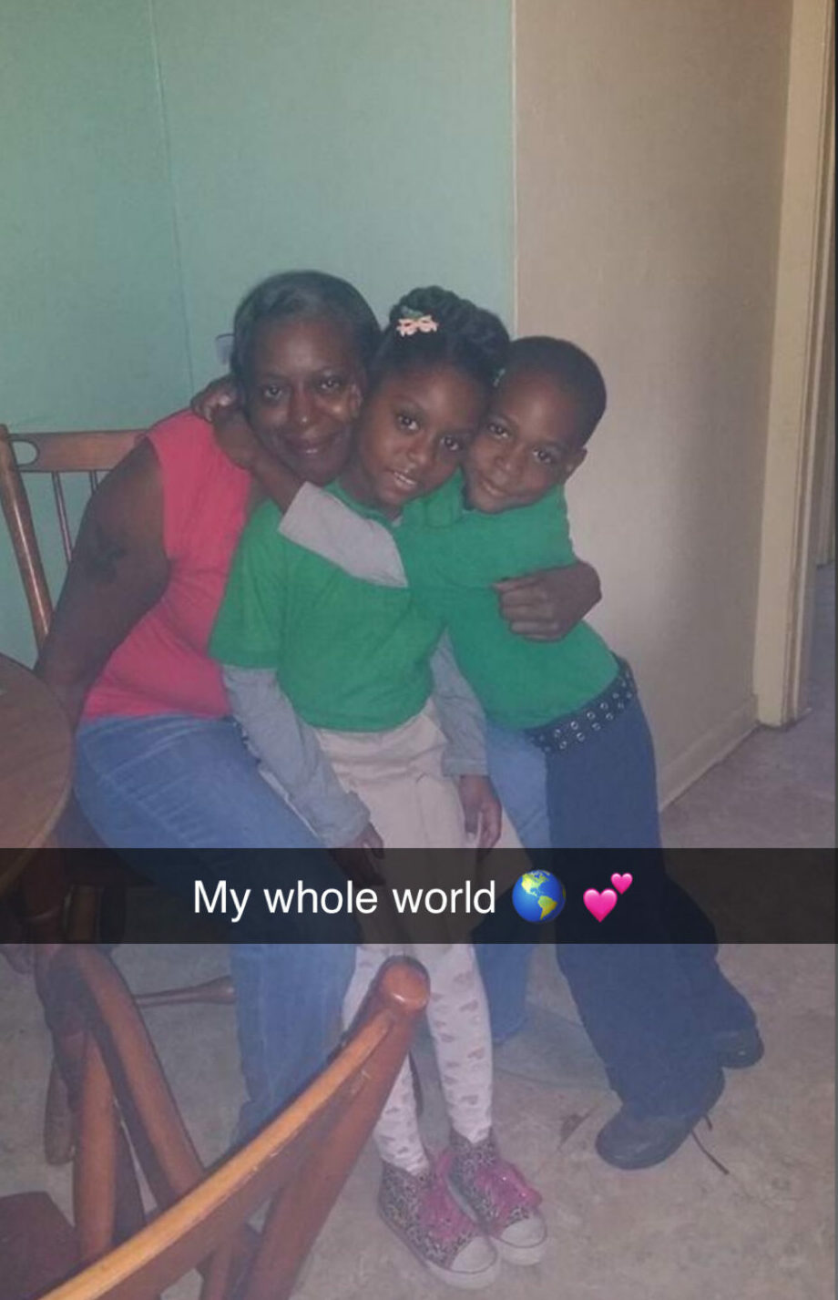 Three children sitting together on a chair, smiling, with a wall background, captioned 'My whole world' with heart and star emojis.