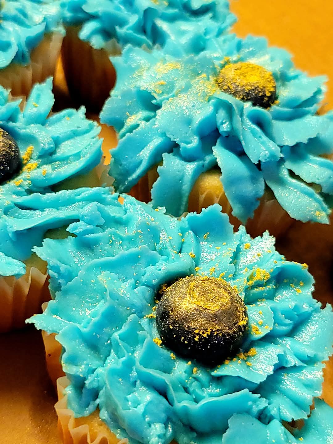 Close-up of cupcakes decorated with blue frosting, black candies, and yellow sprinkles, on a yellow background.