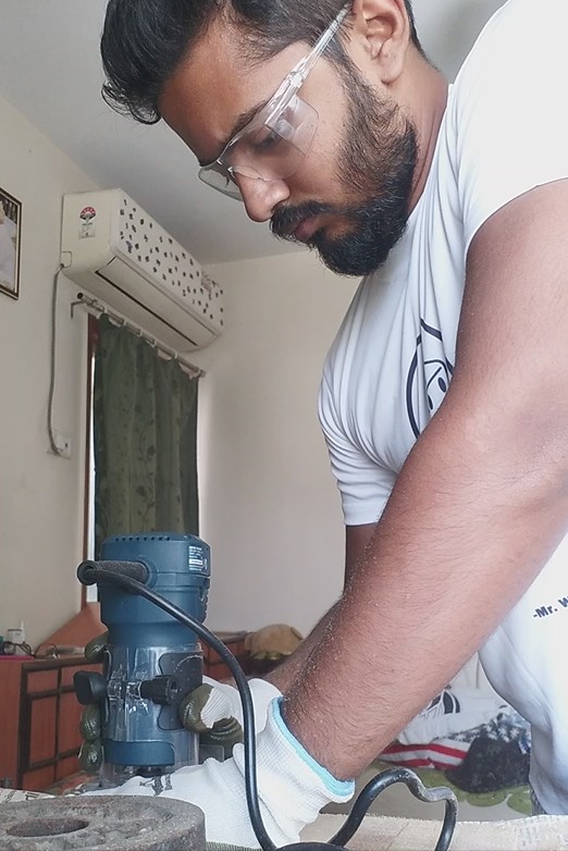 Man wearing safety glasses and gloves working with a power tool on a workbench, focused on his task.