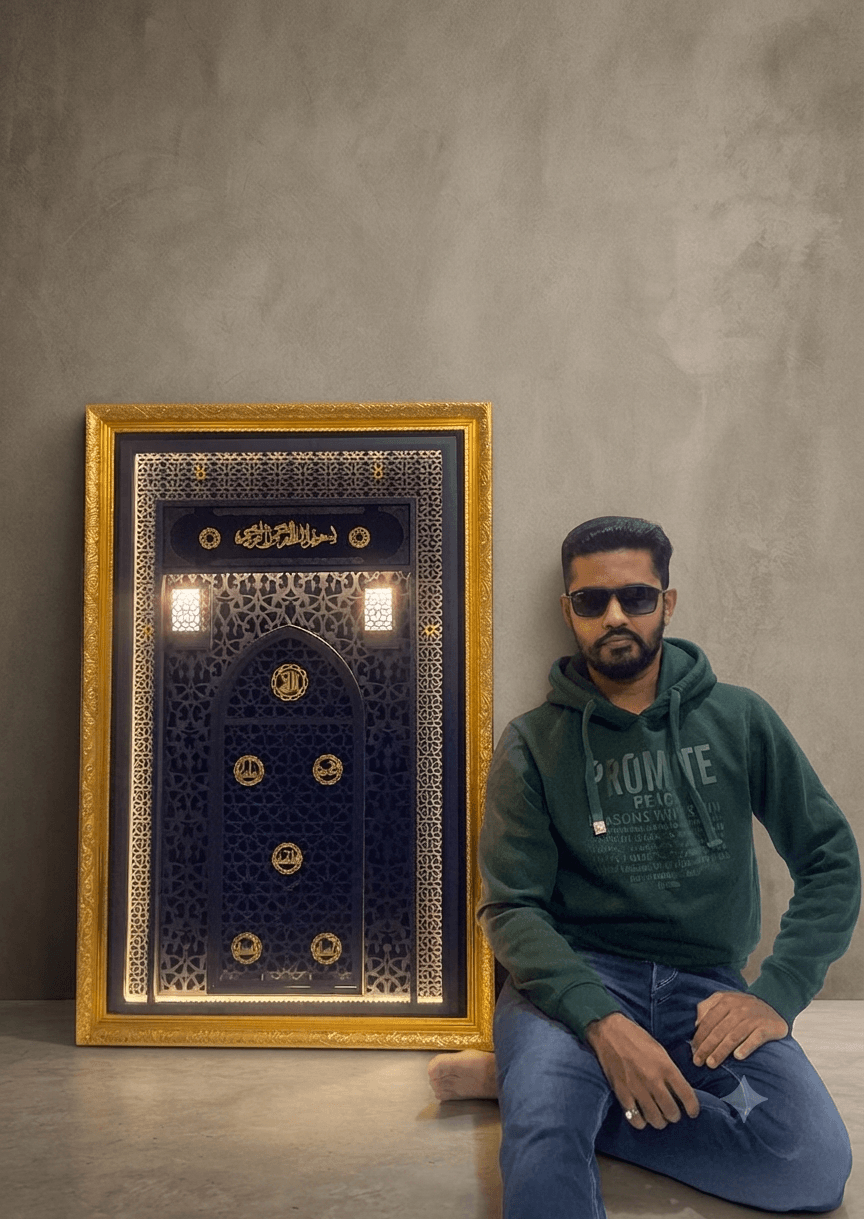 Man with sunglasses and beard sitting on the floor next to a decorative framed mirror or artwork, against a plain wall.